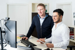 Mitarbeiter Stefan und Paiman besprechen sich vor Computer
